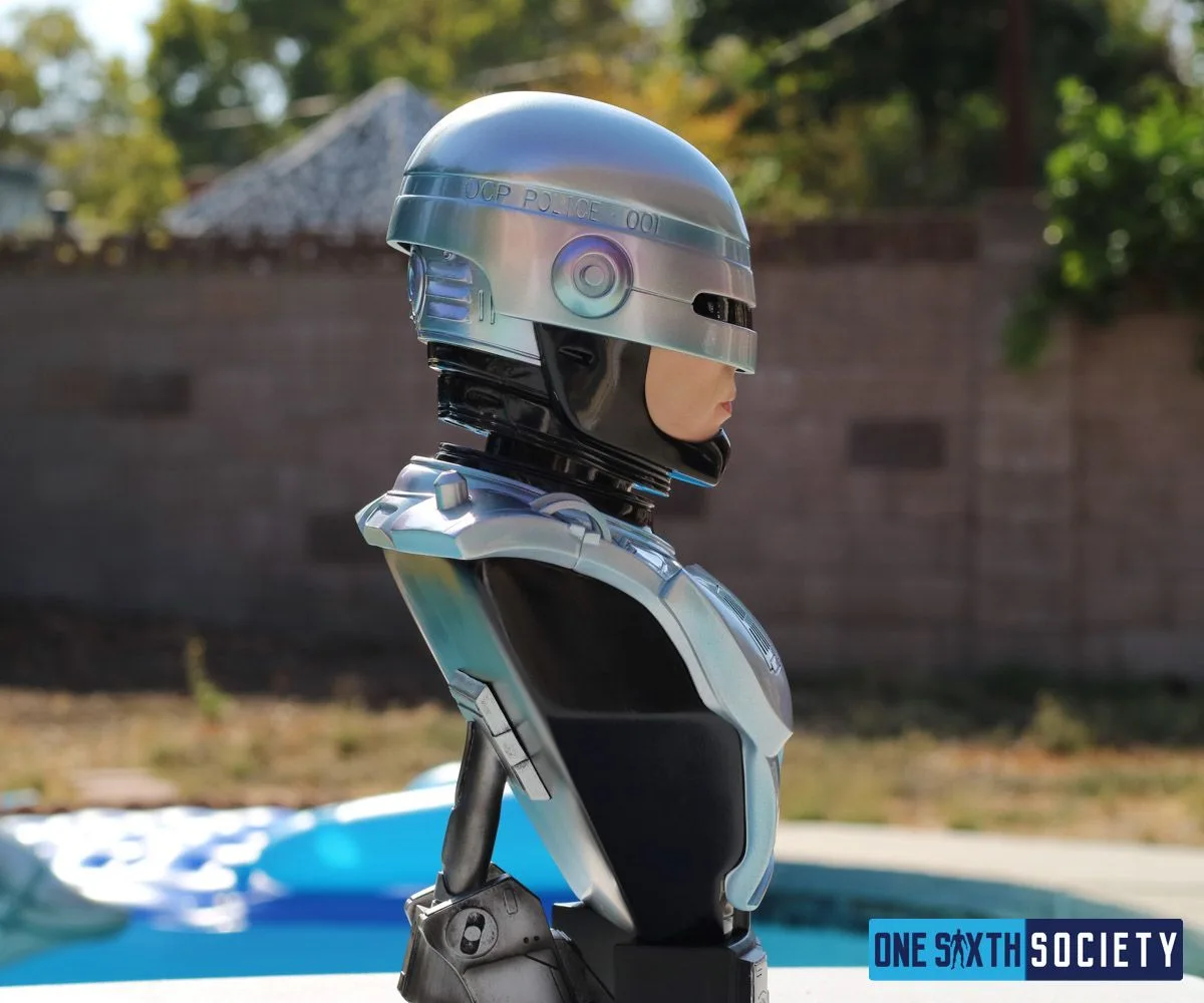 Side view of the RoboCop bust showing the silver-blue helmet, black neck structure and shoulder armor outdoors.