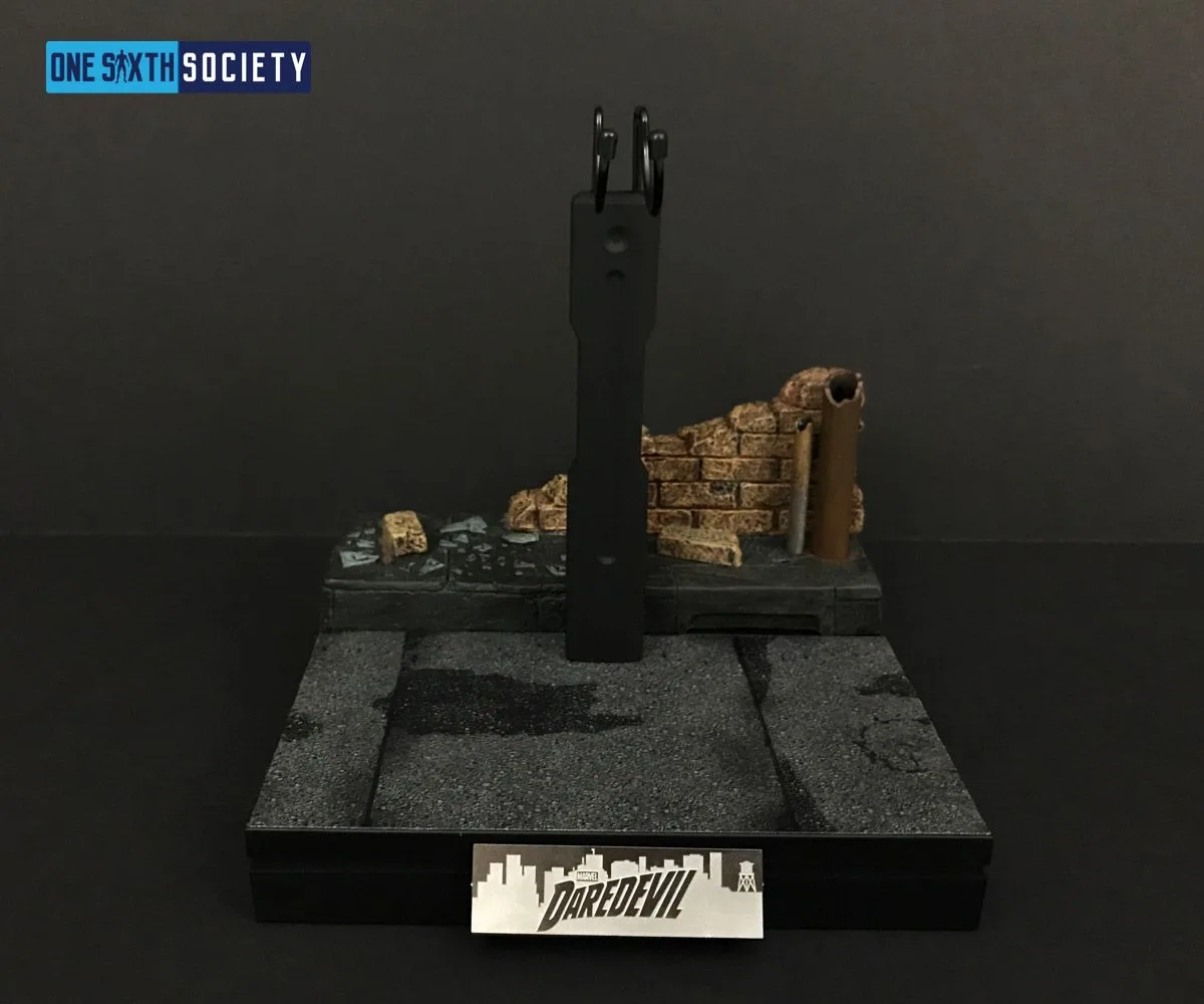 Empty Daredevil rooftop display base with pipes, a brick wall section, vertical figure support and a front nameplate.