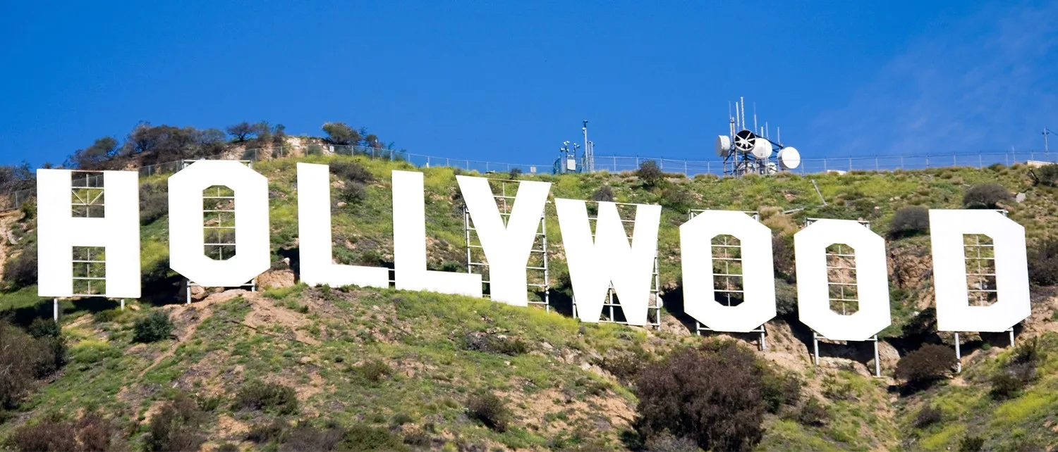 White Hollywood letters stretching across a sunlit hillside beneath a clear blue sky.