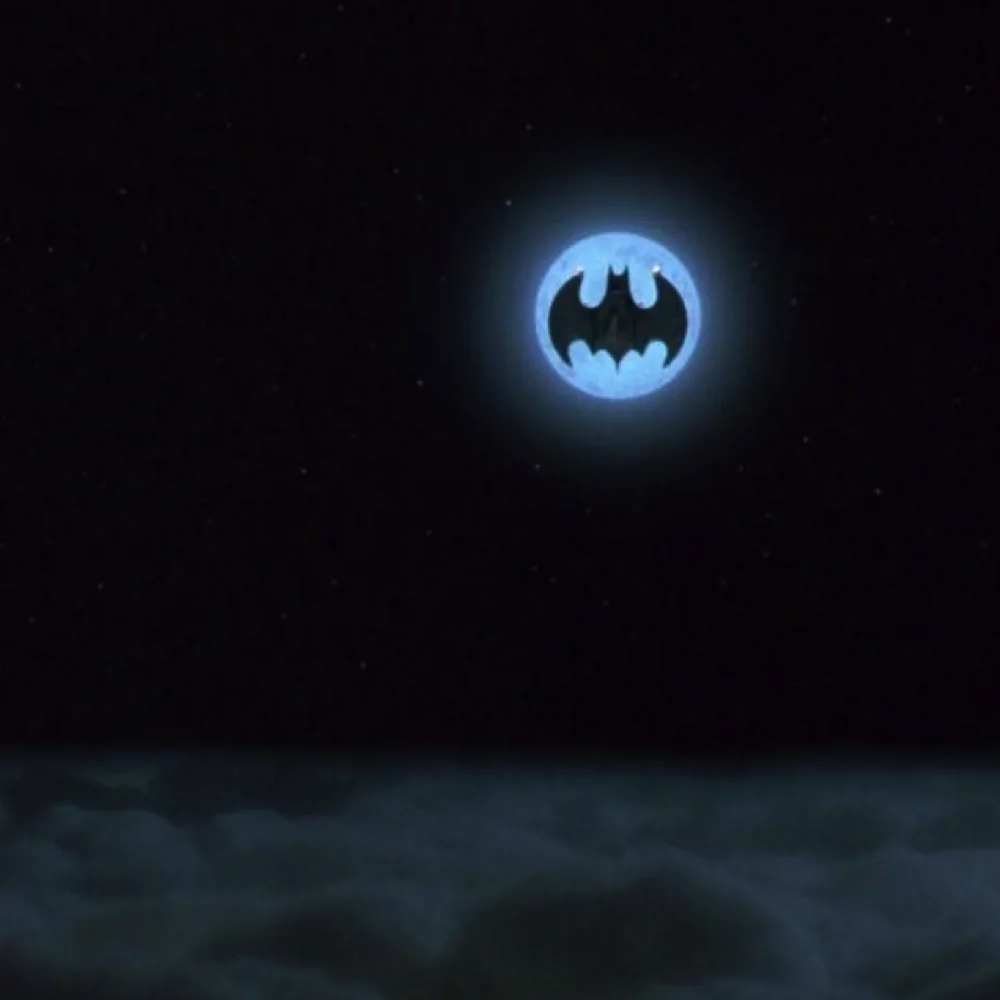 Batwing silhouette centered against a blue full moon above dark clouds in imagery from Batman (1989).