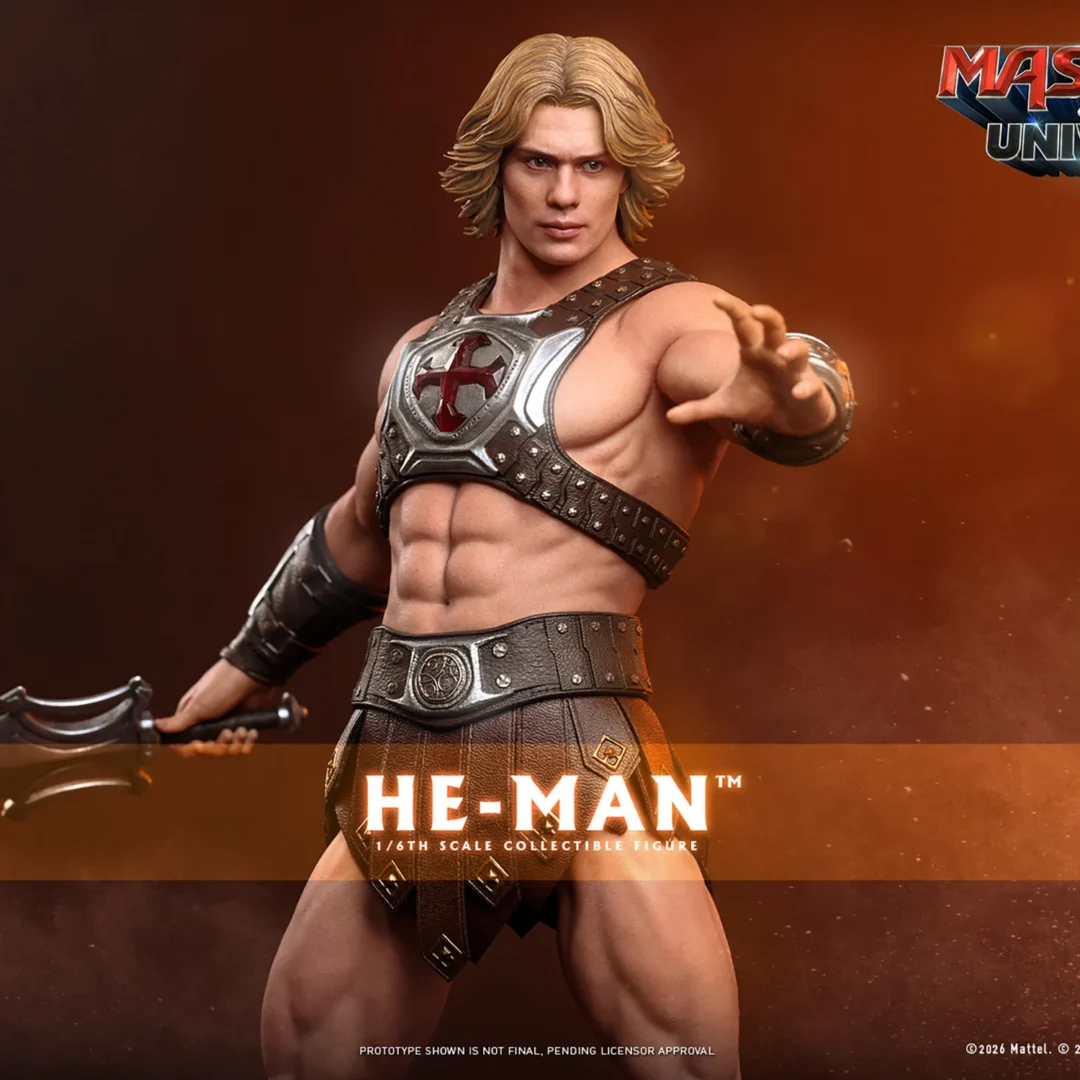 Hot Toys He-Man extending an open hand while holding the Power Sword low at his side, with wavy blonde hair, a silver chest emblem and a muscular bare torso.