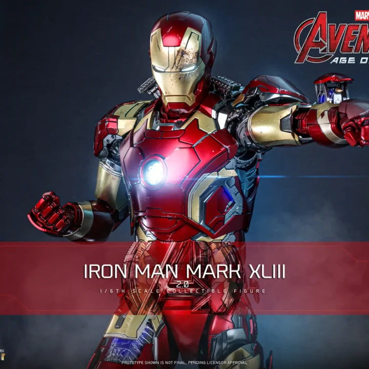 Hot Toys Iron Man Mark XLIII 2.0 aiming one forearm forward, with a deployed wrist weapon and a glowing round arc reactor in the red-and-gold armor.