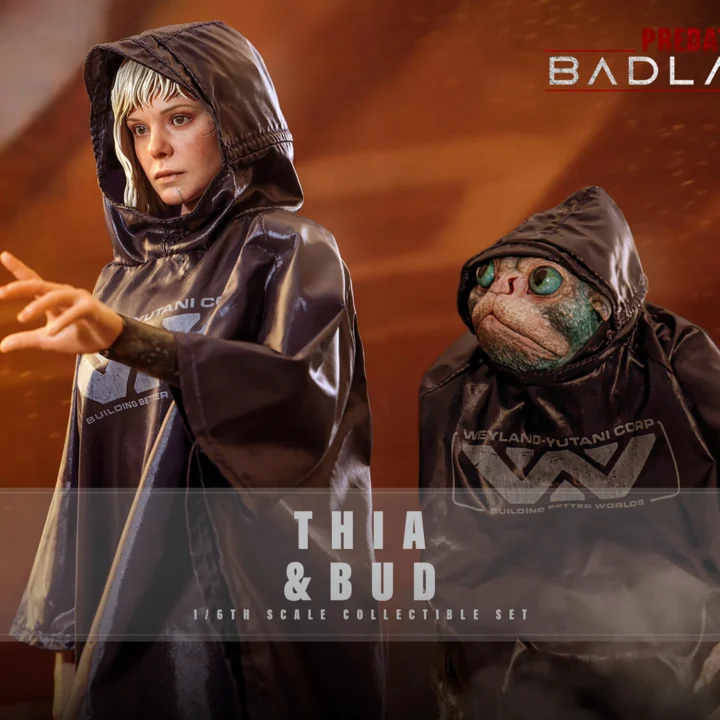 Hot Toys Thia reaching an open hand forward beside Bud, both wearing glossy black Weyland-Yutani raincoats with raised hoods against an orange background.